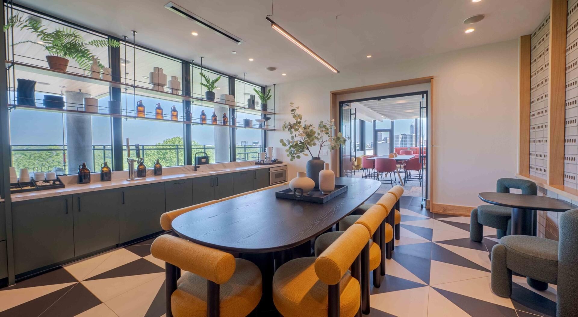Un intérieur moderne avec une longue table à manger, des chaises rembourrées de couleur jaune et une vue sur la ville grâce à de grandes fenêtres.