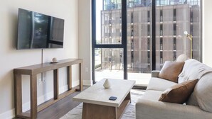 Een moderne woonkamer met een flatscreen televisie, een houten salontafel, een bijzettafeltje en een bank met kussens.