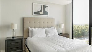 Ein Hotelzimmer mit einem großen Bett, zwei Nachttischen mit Lampen, einem modernen Kopfteil und einem gerahmten Kunstwerk darüber.