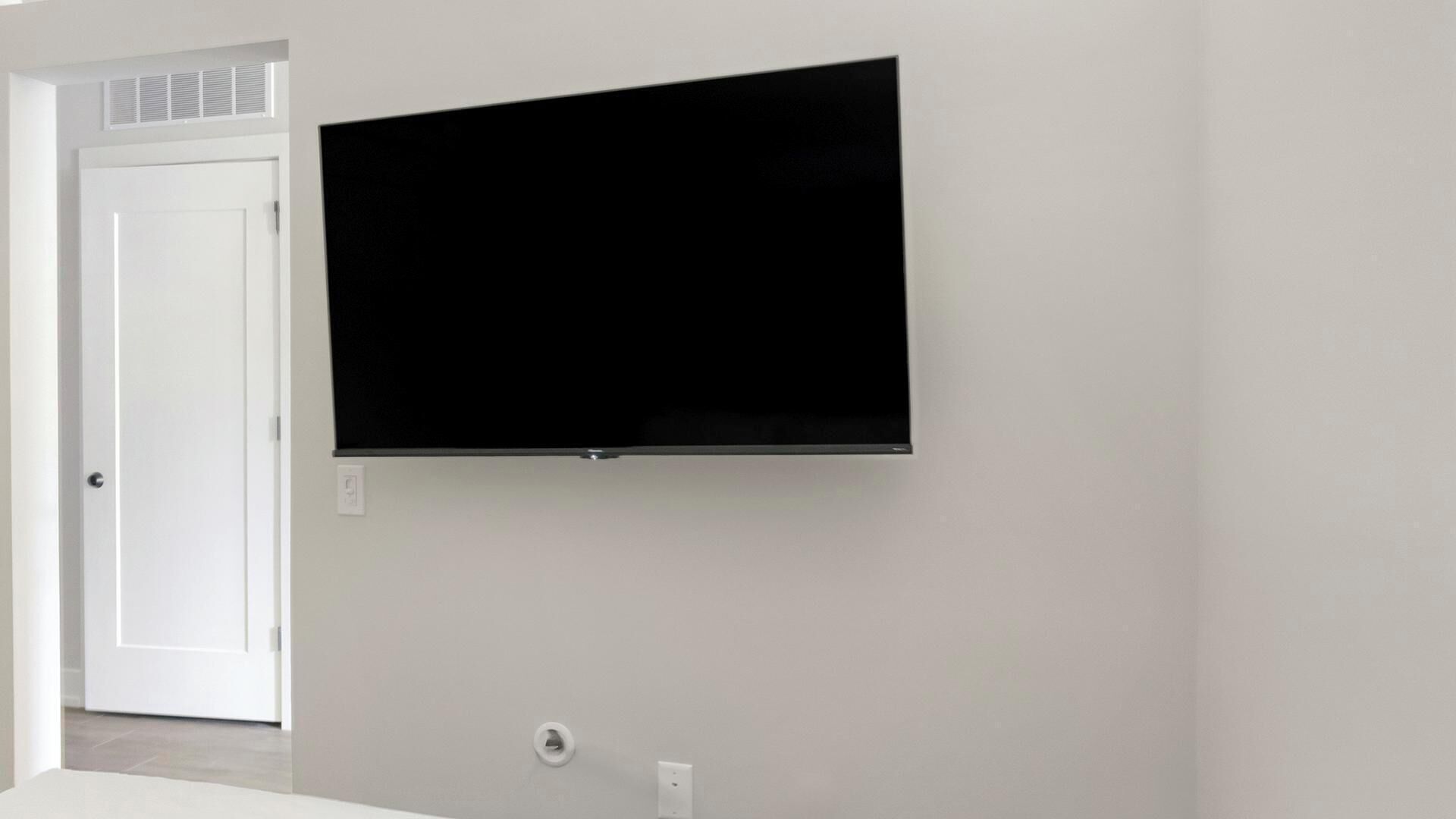 Une pièce avec un téléviseur fixé au mur, une porte blanche et un interrupteur.