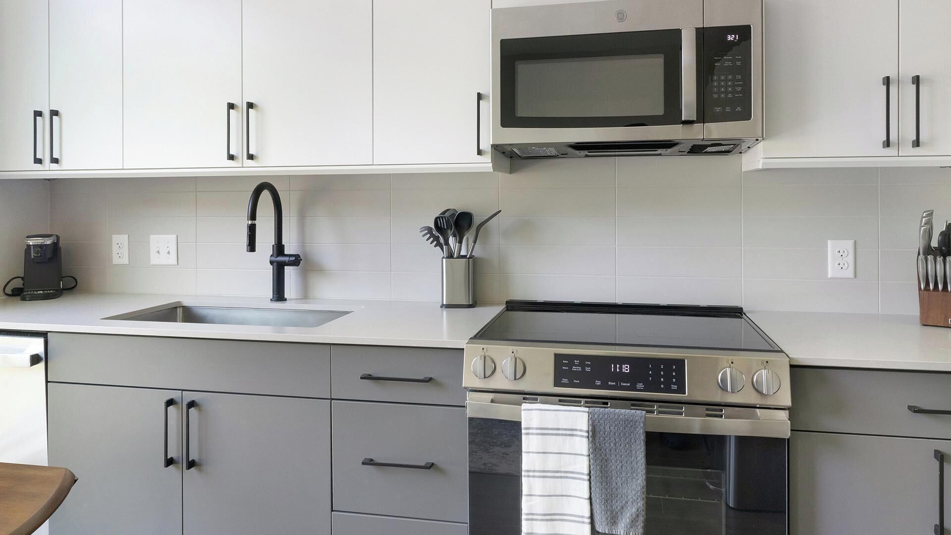 Eine moderne Küche mit einem Edelstahlherd, einer eingebauten Mikrowelle, einer Spüle mit Wasserhahn und einer Kaffeemaschine.