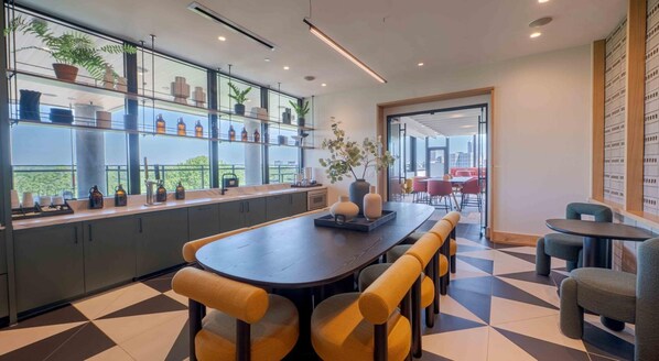 Un intérieur moderne avec une longue table à manger, des chaises rembourrées de couleur jaune et une vue sur la ville grâce à de grandes fenêtres.