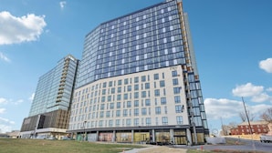 A modern hotel with a curved glass facade, multiple floors, and a flat roof. - Landing | Stunning Studio in Caraleigh (Raleigh)