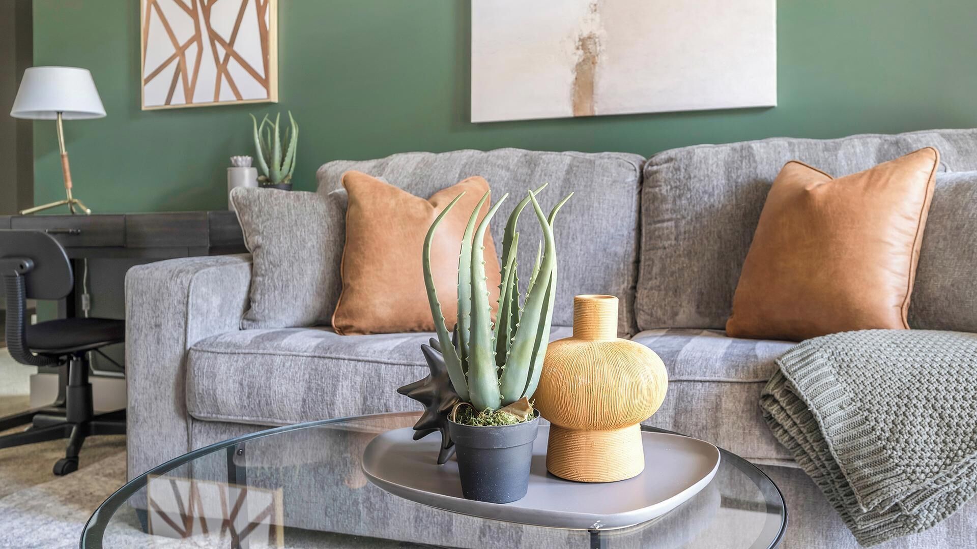 A living room with a grey sofa, a round glass coffee table, a potted plant, and a decorative vase.