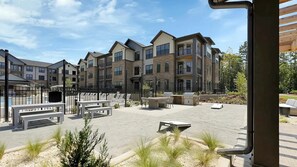 A courtyard with outdoor seating, a barbecue area, and a view of multi-story residential buildings. - Landing | Modern 1BD, Game Room, Gym (Charlotte)