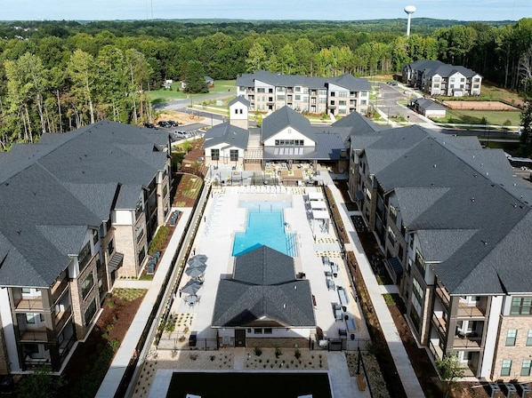 A modern apartment complex with a central swimming pool, multiple buildings, and a surrounding wooded area. - Landing | Spectacular 2BD, Game Room, Gym (Charlotte)