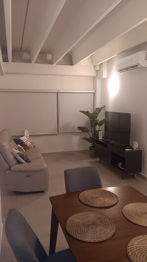 Uma sala de estar moderna com um sofá, uma mesa de jantar com jogos americanos, uma televisão e uma planta.