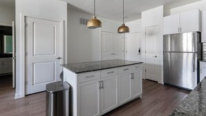 A modern kitchen with white cabinetry, a stainless steel refrigerator, and two pendant lights. - Landing | Chic 1BD, Clubhouse, Gym (Kyle)