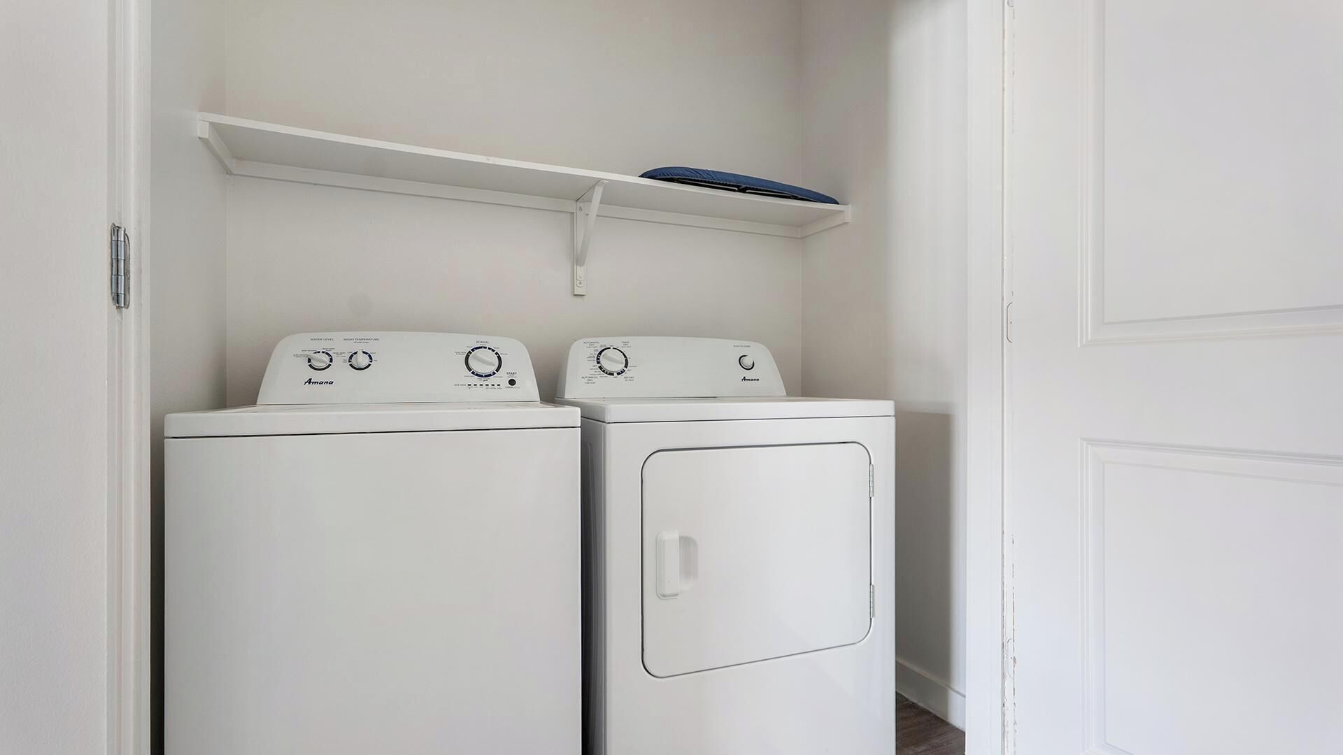 Une buanderie avec deux machines à laver à chargement frontal, toutes deux de couleur blanche, et une étagère placée au-dessus.