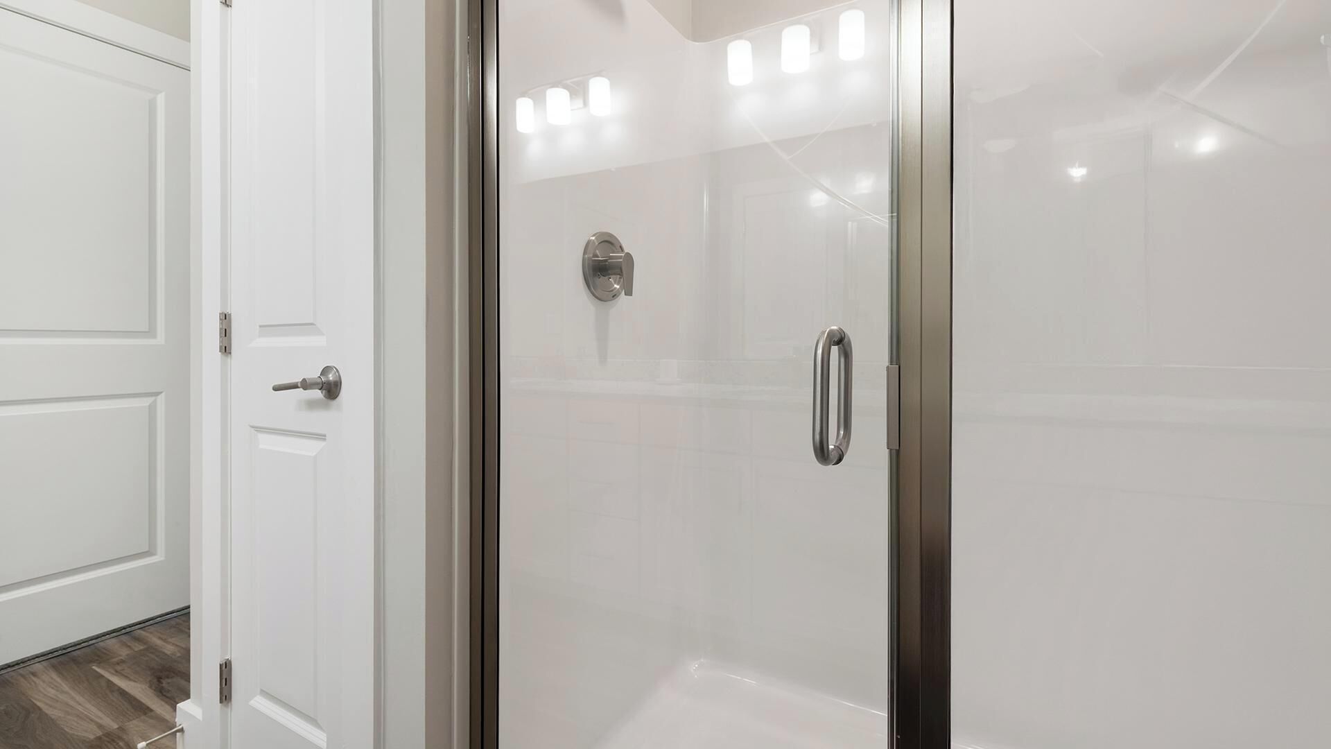 A bathroom with a glass shower enclosure, a white door, and a visible shower control panel.