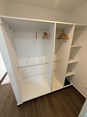 Ein begehbarer Kleiderschrank mit offenen Regalen, einer Kleiderstange und einem Holzaufhänger.