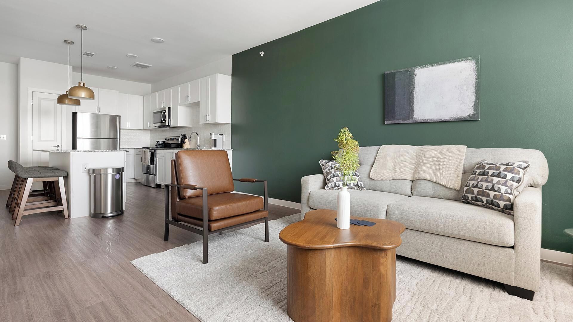 A modern living space with a kitchen, a leather chair, a wooden coffee table, and a grey sofa.
