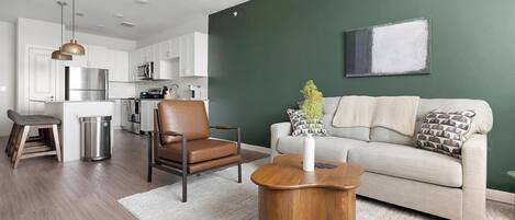 A modern living space with a kitchen, a leather chair, a wooden coffee table, and a grey sofa.