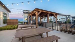 An outdoor patio with wooden benches and string lights. - Landing | Chic 1BD, Gym, Clubhouse (Kyle)