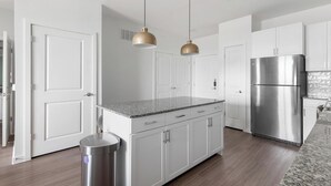 A modern kitchen with white cabinetry, a stainless steel refrigerator, and pendant lighting. - Landing | Chic 1BD, Gym, Clubhouse (Kyle)