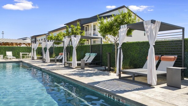 A poolside area with lounge chairs, a swimming pool, and a building with a covered patio. - Landing | Chic 1BD, Gym, Clubhouse (Kyle)