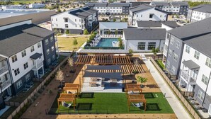 A residential building complex with multiple apartment units, a swimming pool, and a patio area with outdoor seating. - Landing | Chic 1BD, Gym, Clubhouse (Kyle)