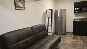 A modern kitchen with a black sofa, a tall floor lamp, and a refrigerator.