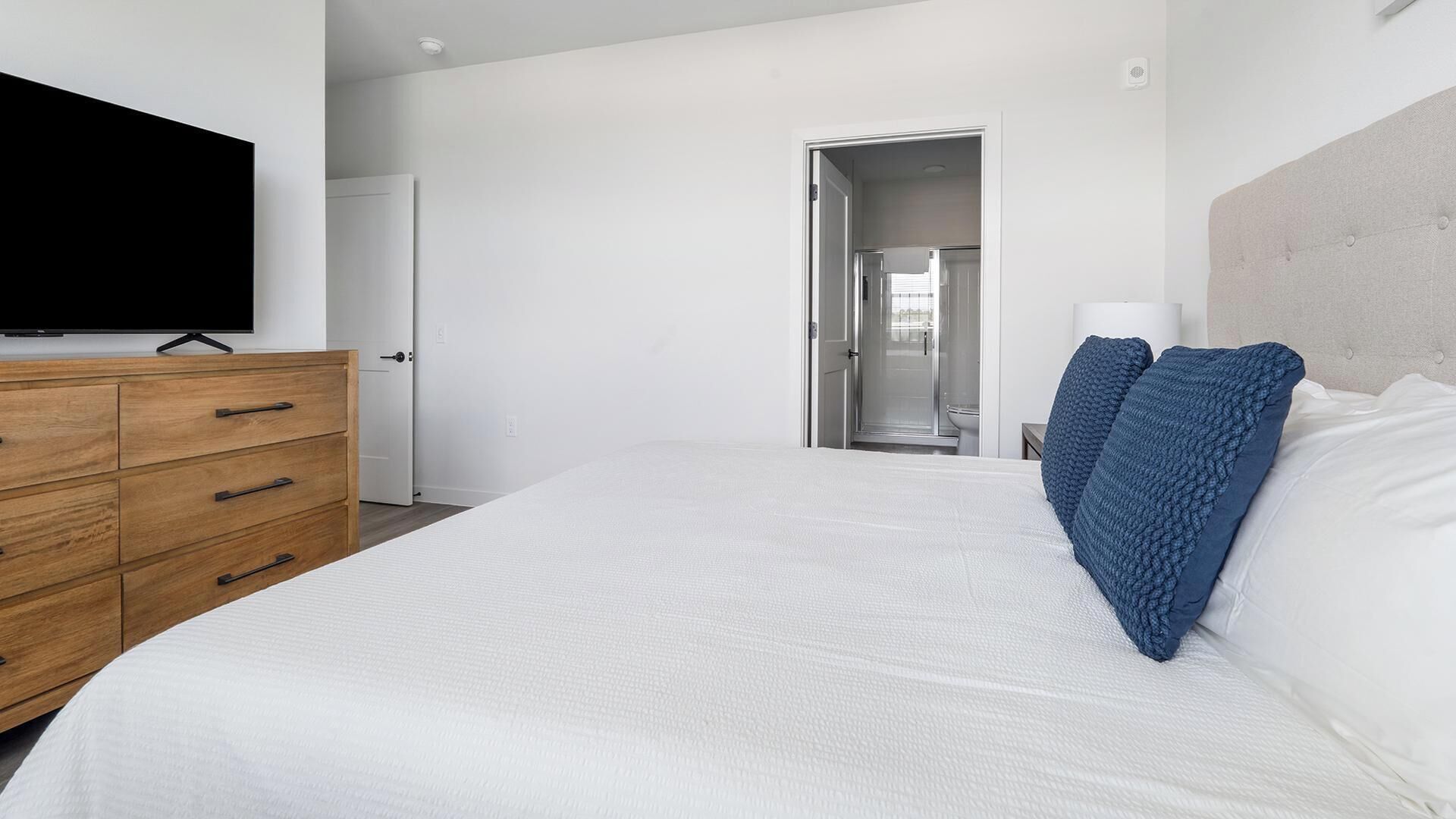 A bedroom with a bed, wooden dresser, and a television on the wall.