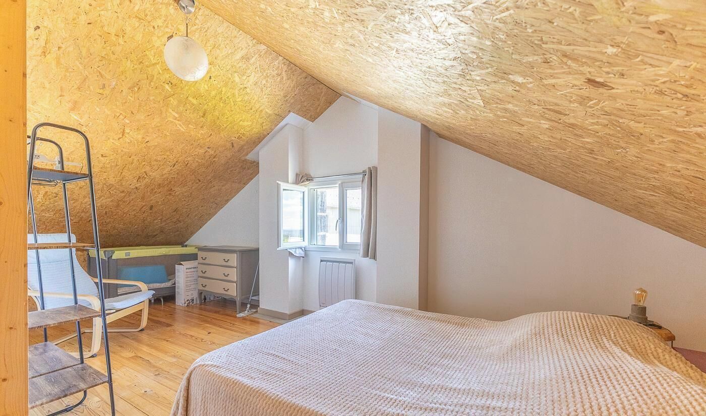 Une chambre avec un plafond en pente, un lit, une chaise, une commode et une fenêtre.