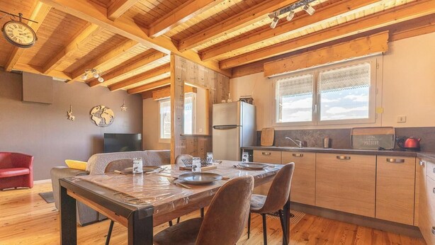 Interior de madeira com uma mesa de jantar, cadeiras, área de cozinha e um relógio na parede.