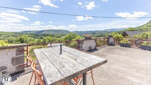 Mesa e cadeiras de madeira num terraço com vista para uma paisagem montanhosa.