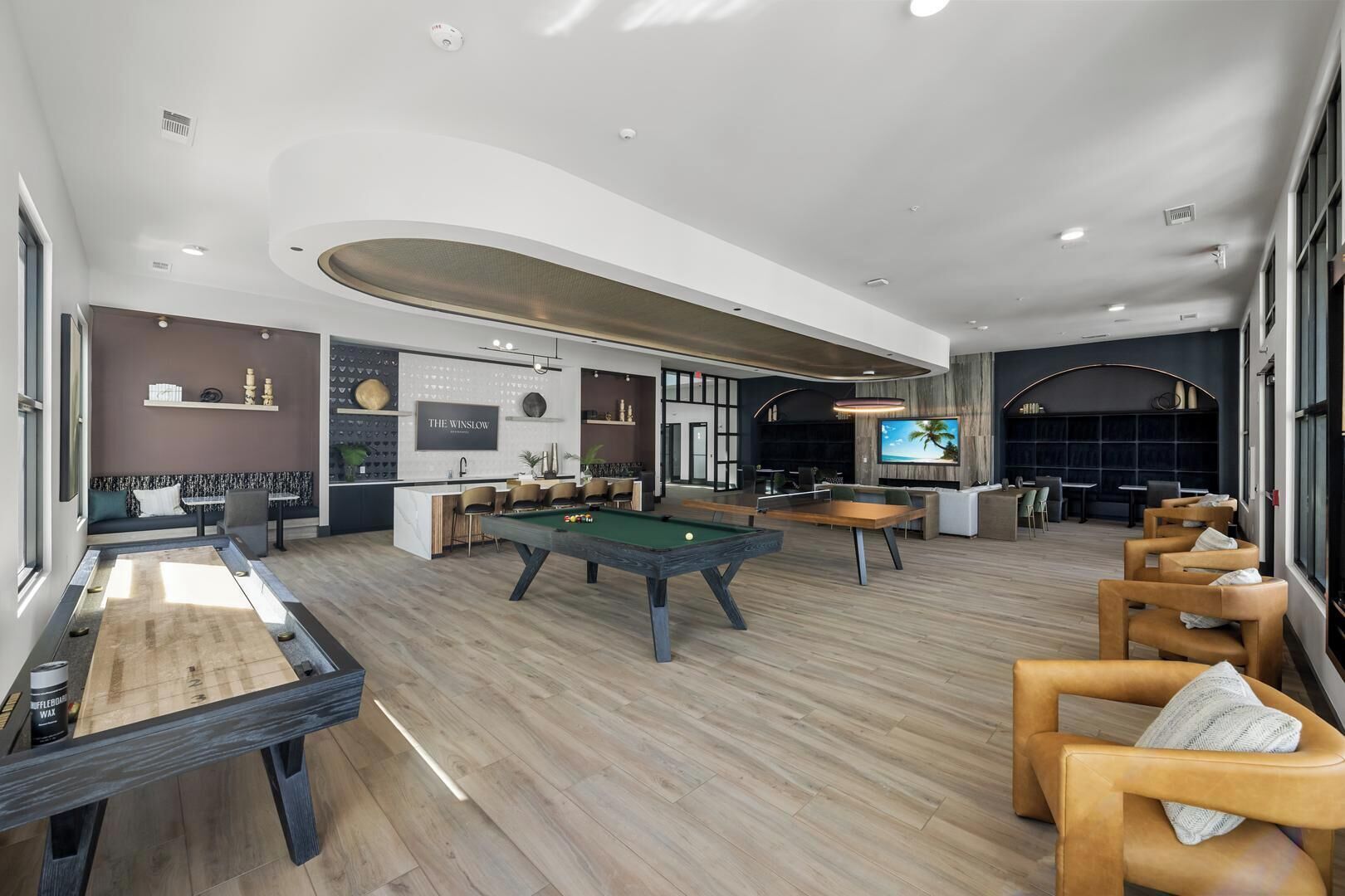 A modern indoor space with a pool table, billiards, a bar area, and seating.