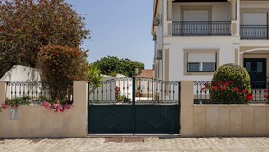 Un edificio a più piani con un ingresso chiuso da cancello, un balcone al piano superiore e un giardino curato con piante in fiore.
