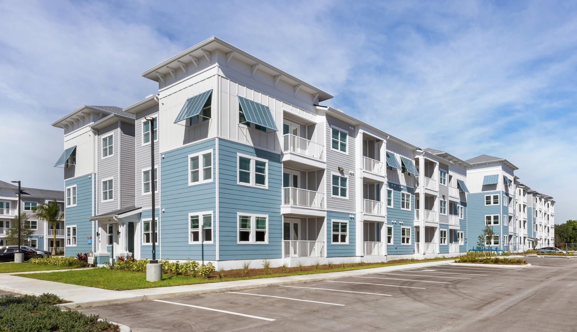A multi-story residential building with balconies, a parking lot, and a clear sky.