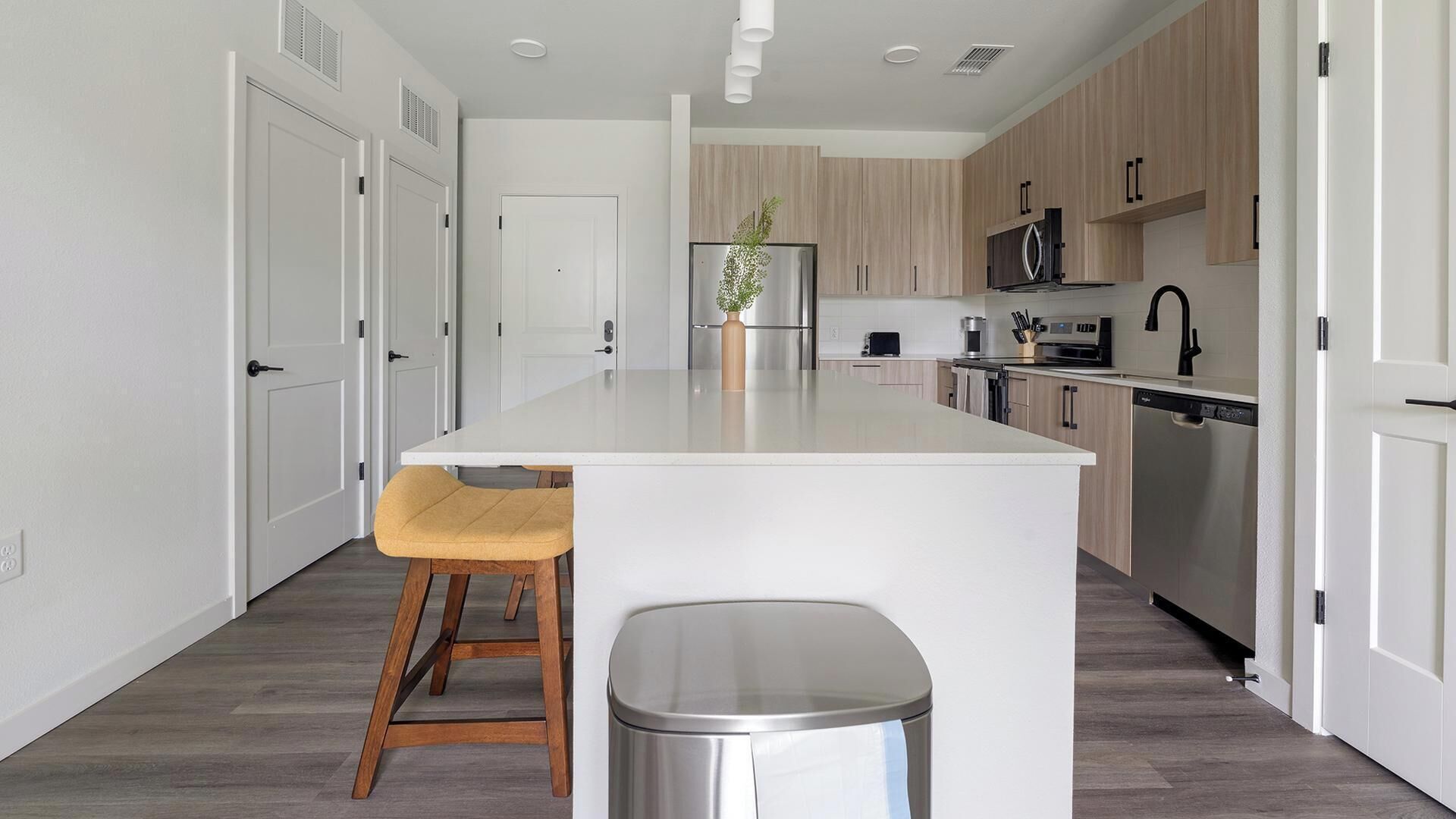 Una cucina moderna con mobili bianchi, un'isola centrale con sgabelli, elettrodomestici in acciaio inossidabile e vista sull'area pranzo adiacente.