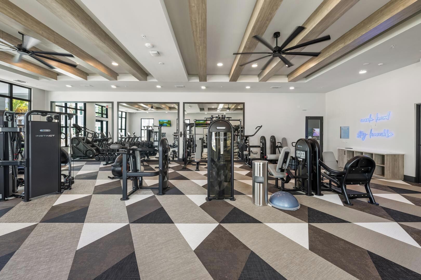 Een sportschool met diverse fitnessapparaten, een zwart-wit schakeerdvloer en een motiverende boodschap op de muur.
