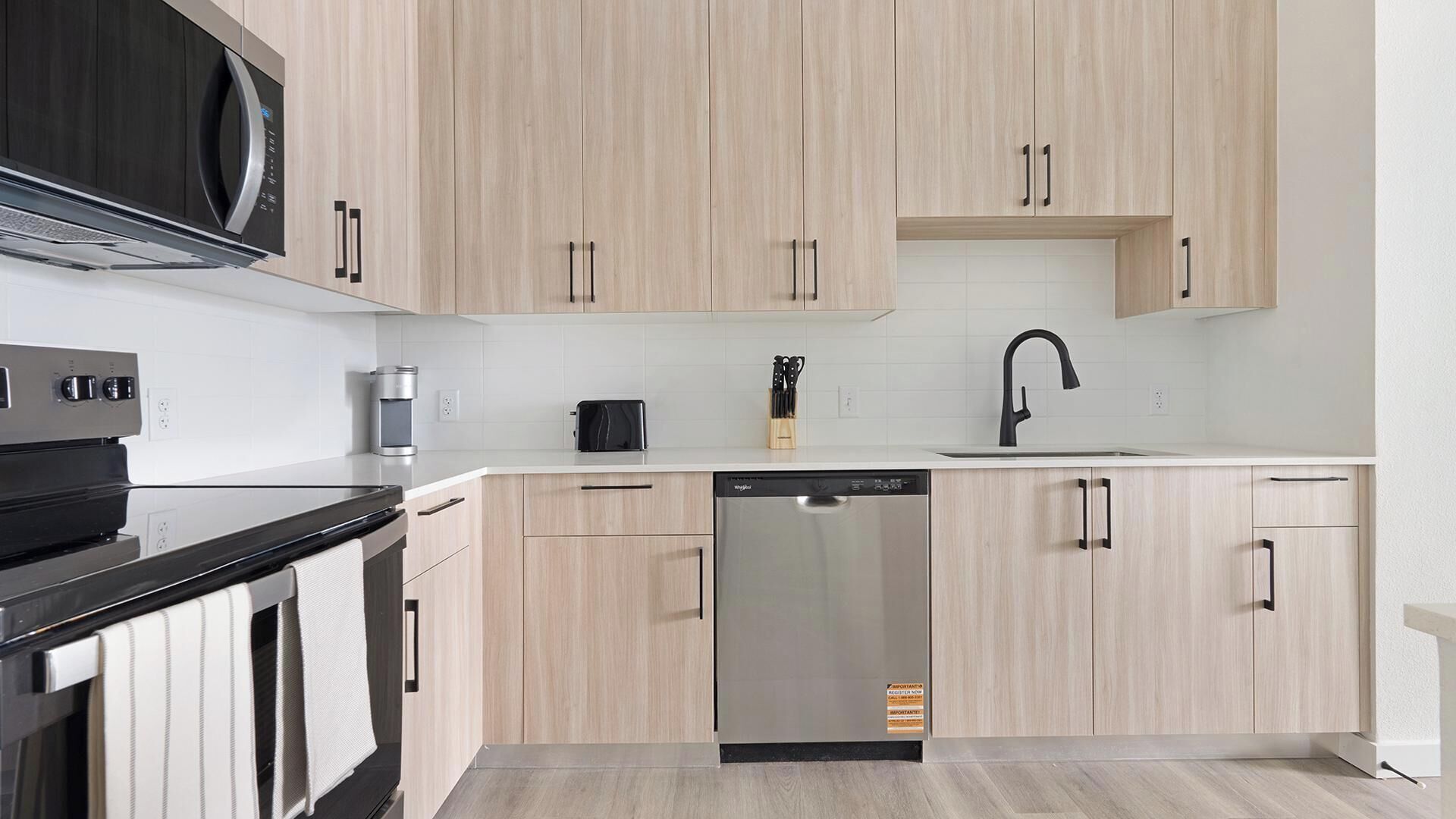 Een moderne keuken met licht houten kastjes, een zwarte magnetron, een koffiezetapparaat en een vaatwasser.