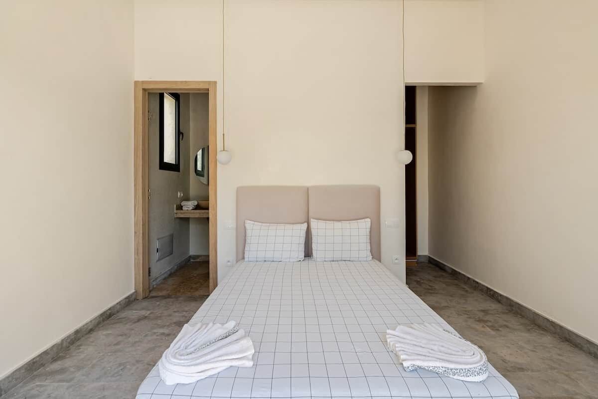 A single bed with a grid-patterned bedspread, two pillows, and a pair of towels on the floor.