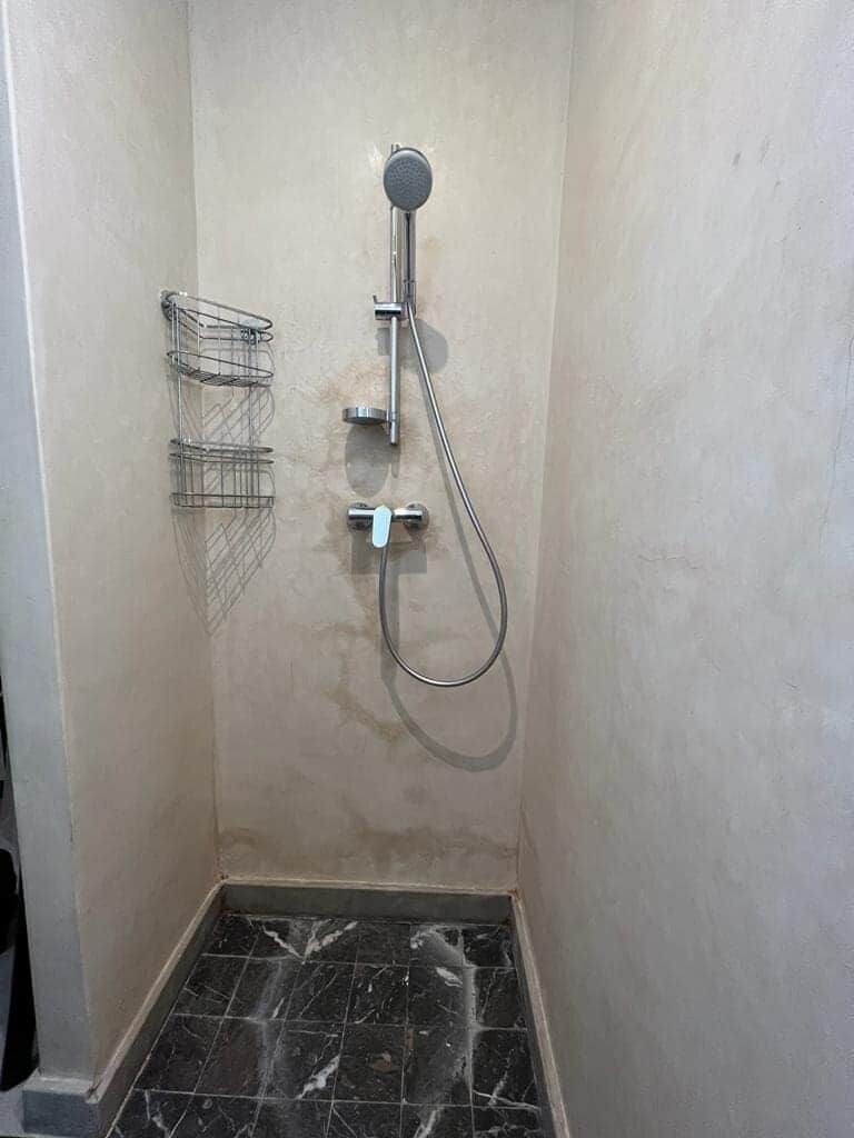 A shower area with a handheld showerhead, a wall-mounted towel rack, and a tiled floor.