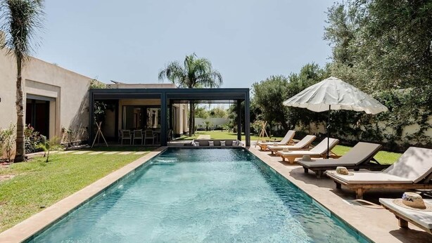 Una piscina con lettini e ombrelloni, immersa nel verde e affiancata da un edificio.
