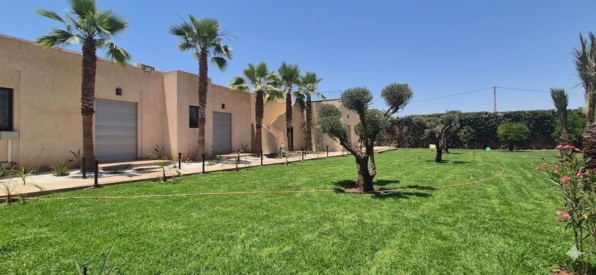 A building with a flat roof, a large garage door, and a well-maintained lawn with palm trees.
