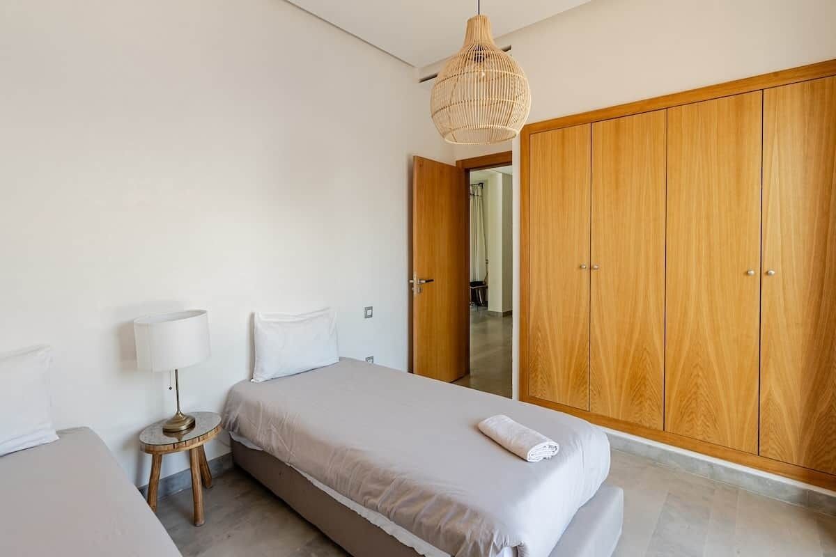 Une chambre à coucher comprenant un lit, une table de chevet, une lampe, une armoire et un luminaire suspendu.