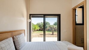 Una camera da letto con un letto, vista su una zona esterna attraverso una porta scorrevole e una porta in legno sulla destra.