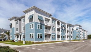 Un edifici residencial de diversos pisos amb balcons, un aparcament i un cel serè.