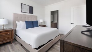 Habitació d'hotel amb un llit, taules de nit, escriptori, mirall i una porta.