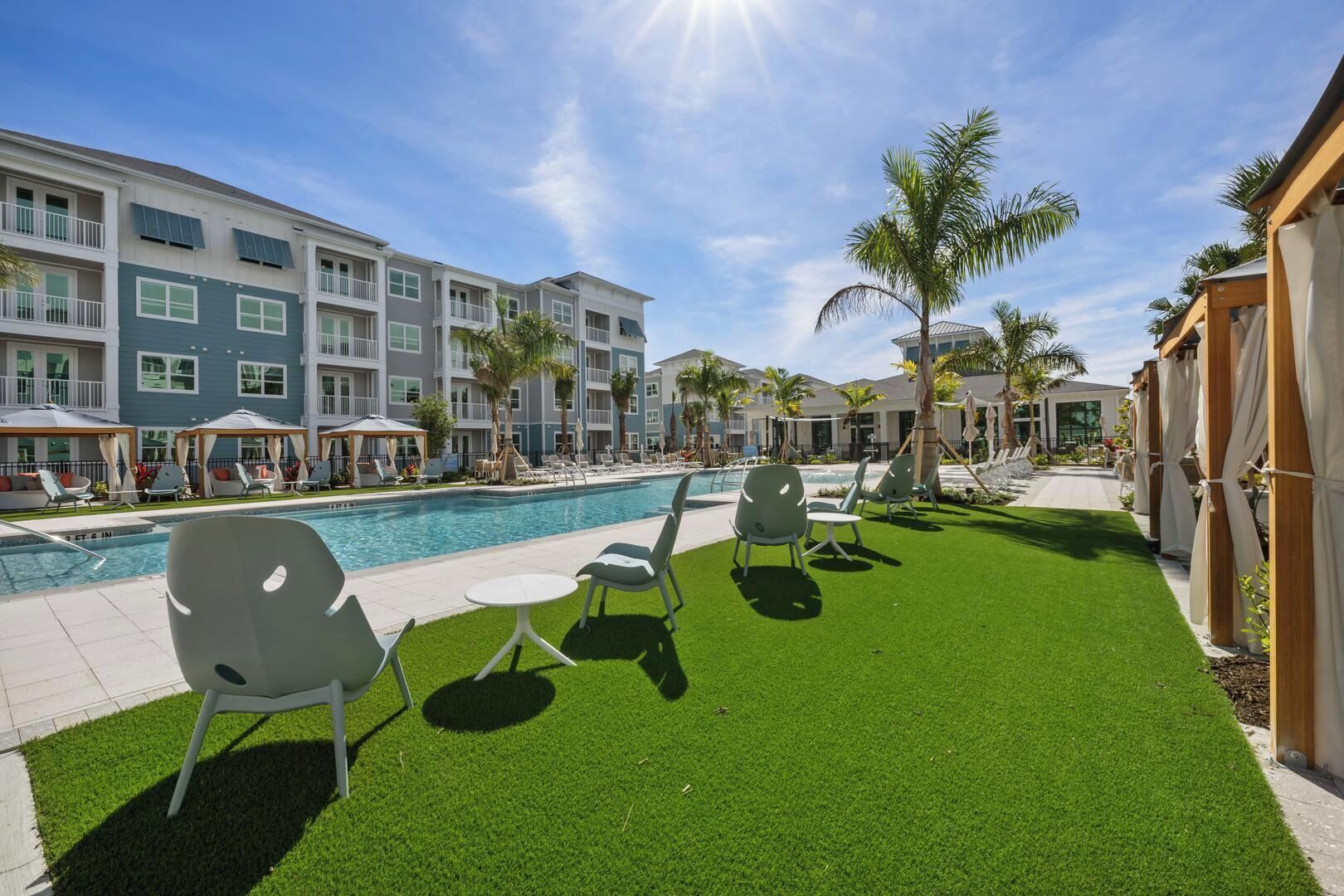 A pool area with artificial grass, lounge chairs, and a building with balconies.