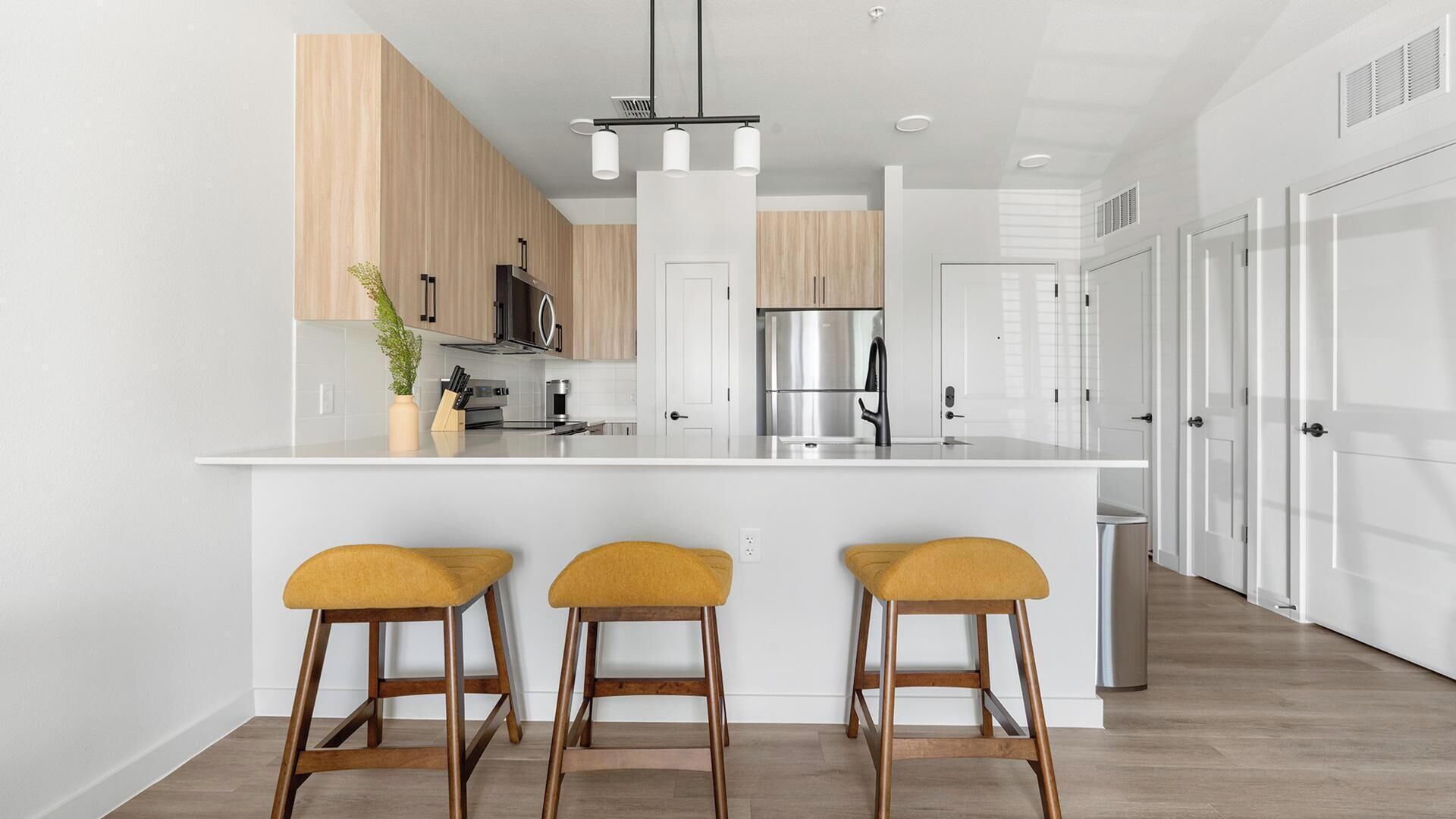 Una cucina moderna con isola centrale, mobili in legno e tre sgabelli da bar.