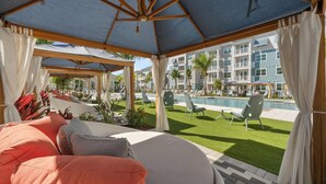 Un espace extérieur aménagé, partiellement abrité, avec vue sur la piscine, comprenant des chaises longues et un bâtiment avec des balcons en arrière-plan.
