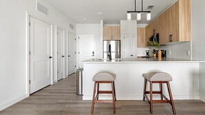 Een moderne keuken met een centraal eiland, houten kastjes en twee barkrukken.