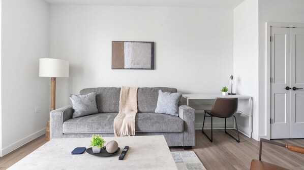 Una sala de estar moderna con un sofá gris, una mesa de centro, una lámpara, un escritorio y una silla.