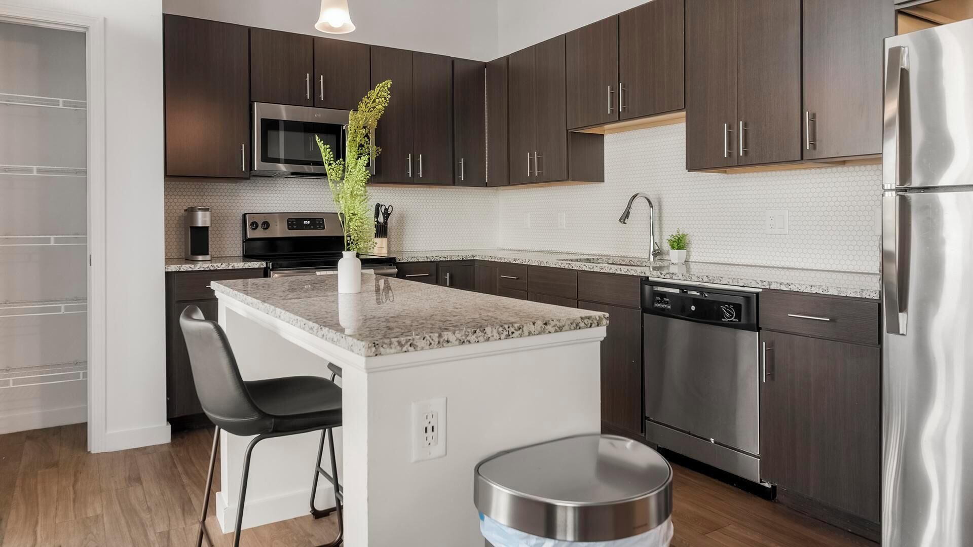 A modern kitchen with dark wood cabinets, stainless steel appliances, a granite countertop, and a small island with seating.