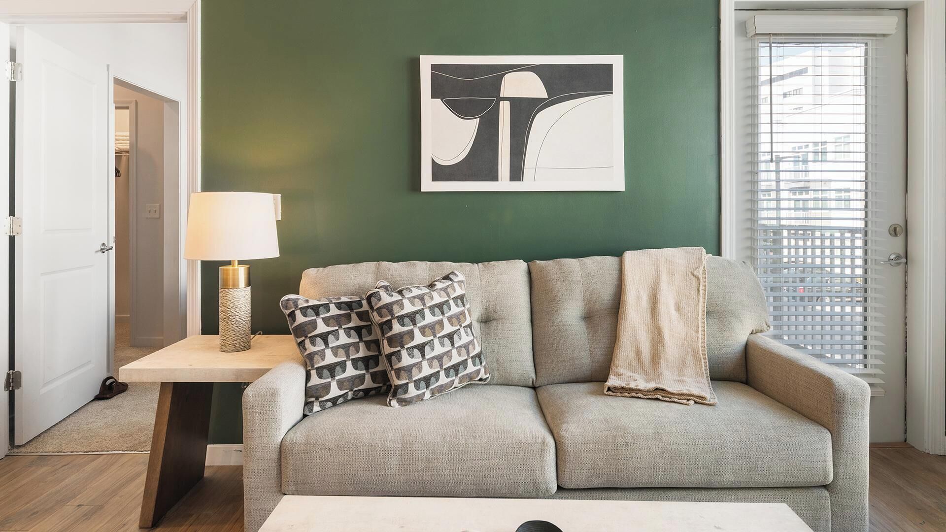 Una sala de estar con un sofá, una lámpara, un cojín estampado, una manta y una obra de arte enmarcada en la pared.