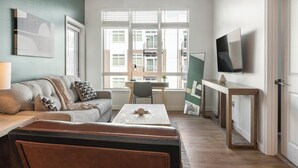 Ein modernes Wohnzimmer mit einer Couch, einem Couchtisch, einem Fernseher und Blick auf die Stadt durch große Fenster.