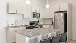 Una cocina moderna con armarios blancos, electrodomésticos de acero inoxidable, encimera de granito y una isla central con asientos.