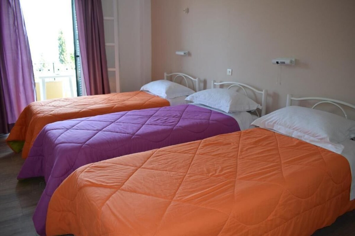 Ein Hotelzimmer mit drei Betten, jedes mit einer andersfarbigen Bettdecke.
